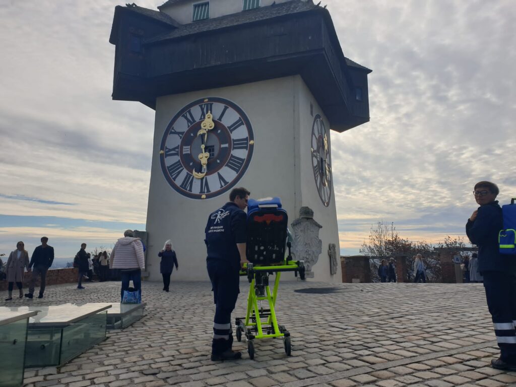 Wunscherfüller mit Fahrgast auf Rettungstrage am Schlossberg mit Blick auf den Uhrturm in Graz